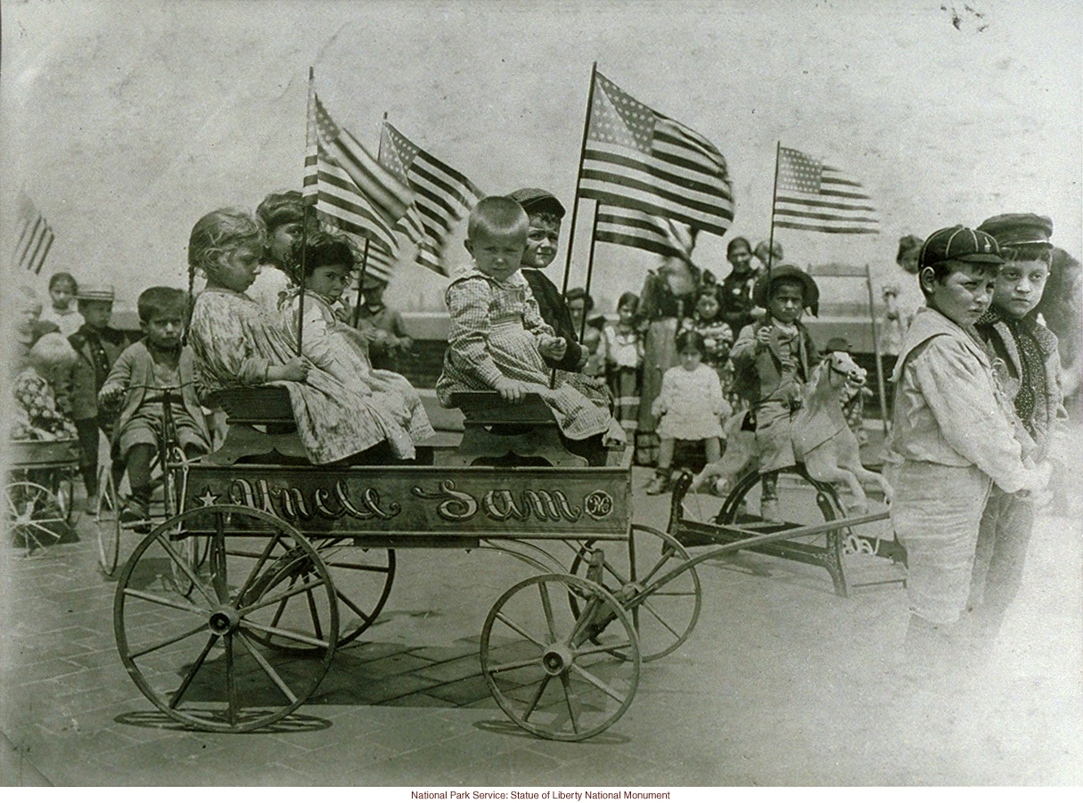 Immigrant children on &quote;roof garden&quote; playground at Ellis Island, with &quote;Uncle Sam&quote; cart (Photograph by Augustus Sherman)