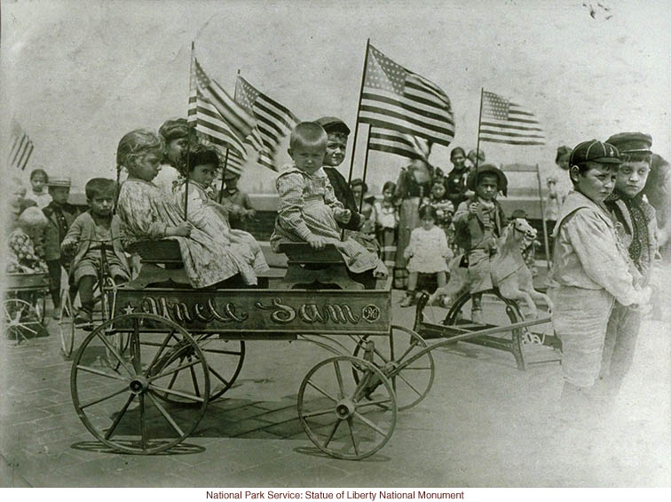 Immigrant children on &quote;roof garden&quote; playground at Ellis Island, with &quote;Uncle Sam&quote; cart (Photograph by Augustus Sherman)